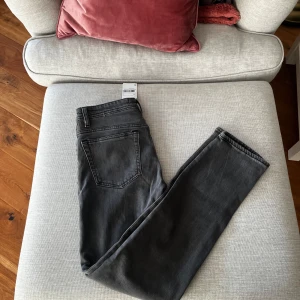 Grå jeans slim fit från Mango  - Snygga grå jeans från Mango Man i slim fit. Klassisk femficksdesign, bälteshällor och knappgylf. Jeansen är tillverkade i bomull och har en stilren, mörkgrå tvätt som passar till allt. Perfekta för dig som gillar en enkel och clean look.