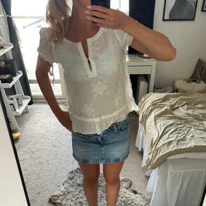 Vit blus från Odd Molly med spets - Supersöt vit blus från Odd Molly med broderade detaljer och volangkant nertill. Blusen har korta ärmar, v-ringning med knapp och romantisk spets längs kanterna. Perfekt för dig som gillar en feminin och luftig stil.