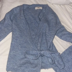 Blå omlottkofta från Gina Tricot XS - Mysig blå kofta från Gina Tricot i ullblandning. Omlottmodell med knytband i midjan och långa ärmar. Perfekt för lager-på-lager och chill dagar. Snygg ribbad kant längs öppningen och mjuk känsla. Storlek xs passar s 