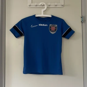 Blå Nike Eskilstuna United fotbollströja - Blå fotbollströja från Nike med Eskilstuna United-logga på bröstet och vit Nike-logga. Tröjan har svarta och vita detaljer på ärmarna och är tillverkad i Dri-Fit-material som andas. Perfekt för träning eller match. Den har lite noppror på vissa ställen (se bild 4) men annars i fint skick.
