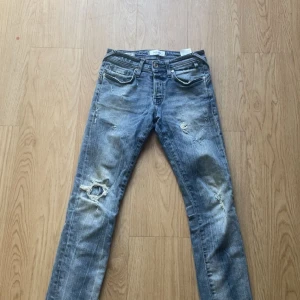 Slim fit jeans från Jack & Jones - Snygga blå slim fit jeans från Jack & Jones, modell Glenn. Jeansen har slitna detaljer och hål på benen för en cool, avslappnad look. Klassisk femficksmodell med dragkedja och knapp. Perfekta för dig som gillar streetstyle.
