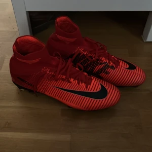 Nike mercurial röda  - Säljer ett par riktigt snygga röda Nike fotbollsskor med svarta detaljer och coolt randigt mönster. Skorna har högre skaft för extra stöd, snörning och plös med Nike-logga. Perfekta för dig som vill sticka ut på planen.                  Vid fundering hör av dig// William 
