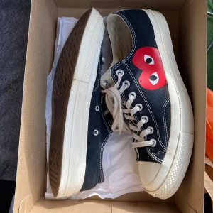 Converse x Comme des Garçons Play sneakers - Svarta Converse x Comme des Garçons Play sneakers med den ikoniska röda hjärtloggan på sidan. Låga sneakers i canvas med vita snören, vita gummisulor och klassisk rund tå. Perfekta för dig som vill ha en streetstyle-vibe med en twist.