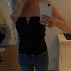 Svart tubtopp med v-ringning Boohoo - Snygg svart tubtopp från Boohoo med markerad v-ringning framtill. Toppen är axelbandslös och har en stilren, tight passform som sitter snyggt på kroppen. 🌸