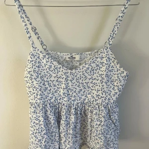 Blommig topp  - Säljer denna supersöta vitblommiga toppen från hollister för att den inte kommer till användning. Toppen har en liten resor i mitten med volang nedtill. 