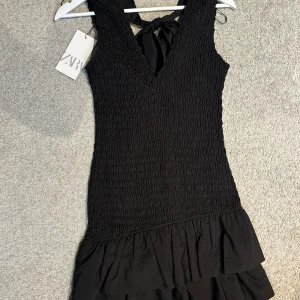 Svart klänning från Zara - Supersnygg svart kort klänning med volanger och en rosett från Zara. Prislapp kvar! Nypris 500kr