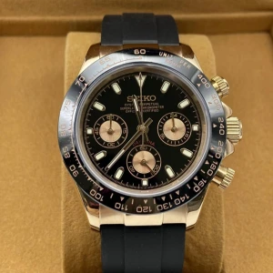 Seiko Daytona-inspirerad klocka svart/guld - Stilren Seiko-klocka med svart urtavla, guldiga detaljer och tre subdials. Boetten är i guldton och armbandet är svart och sportigt i syntetmaterial. Klockan har tydliga index och kronograf-funktion, perfekt för dig som gillar en lyxig och modern look.