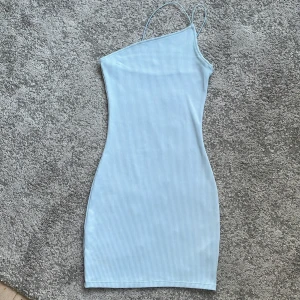 Ljusblå ribbad kortklänning XS - Supersöt ljusblå ribbad kortklänning med smala axelband och asymmetrisk one shoulder-design. Tight passform som framhäver figuren och perfekt för varma dagar. Enkel men trendig stil som är lätt att matcha med sneakers eller sandaler.