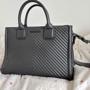 Karl Lagerfeld: Grå quiltad handväska  - Snygg svart handväska från Karl Lagerfeld i quiltat mönster. Väskan har både handtag och avtagbar axelrem. Stilren design med diskret logga framtill och silverfärgade detaljer. Nästan oanvänd 