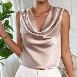 Champagnefärgad satinblus med drapering - Snygg ärmlös blus i champagnefärgad satin med draperad urringning. Perfekt för dig som gillar en elegant och trendig look. Blusen har en mjuk glans och faller snyggt mot kroppen.