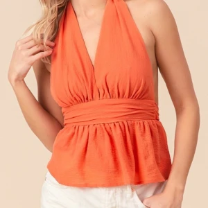 Orange omlott halterneck topp - Snygg orange halterneck topp med omlott och bred midjedetalj. Toppen har djup v-ringning och är ärmlös, perfekt för varma dagar. Den har en lätt rynkad effekt och luftig passform nedtill.