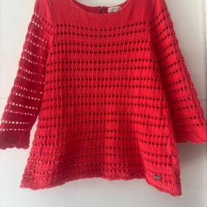 Korall stickad tröja från Cappuccini XL - Korall stickad tröja från Cappuccini i storlek XL. Tröjan har ett genomgående hålmönster, trekvartsärmar och en snygg dragkedja i ryggen. Perfekt för dig som gillar en luftig och unik look. Snygg detalj med metallogo nertill. Storlek är förminskad som M, bröst 96cm, längd 62cm. Bomull 100%