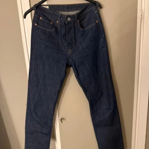 Levi's 501 mörkblå jeans straight fit - Klassiska Levi's 501 jeans i mörkblå denim med raka ben och hög midja. Snygga kontrastsömmar, fem fickor och knappgylf. Perfekta för dig som gillar tidlös stil och vill ha ett par jeans som alltid funkar.