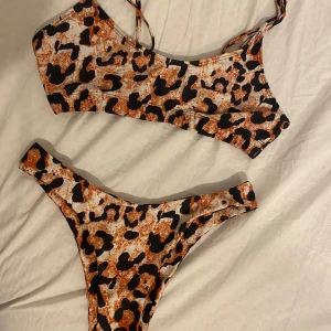 Leopard bikini med smala band - Snygg bikini med leopardmönster i svart och brunt på vit botten. Toppen har smala axelband. Underdelen är brazilian/ string bikini. Perfekt för stranden eller poolen om du vill sticka ut. Strl L men känns som S och M. Underdelen är endast använd en gång medan överdelen är använd flera gånger.
