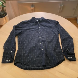 Mönstrad svart skjorta från Filippa K - Svart skjorta från Filippa K med vitt mönster. Mkt fin och dyr skjorta säljes billigt 😁. Skjortan har klassisk krage, vita knappar och långa ärmar med dubbla knappar vid manschetten. Snygg och stilren modell i mjukt bomullstyg. Använd fåtal gånger därav få tecken på användning👍🏼Inköpspris ca 1000. Mitt pris: 350💪 