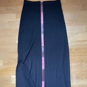 Svart ribbad lång kjol slit  - Säljer en svart ribbad lång kjol från SHEIN i storlek S. Kjolen har en smal passform och materialet är stretchigt och bekvämt. Kan även användas som bandeauklänning. Ett slit vid ena benet