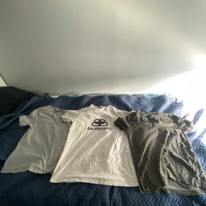 T-shirtpaket Balenciaga & Armani - Säljer tre snygga t-shirts: en vit Balenciaga med svart logga, en grå basic Ralph lauren och en olivgrön Emporio Armani med diskret randigt mönster och knappar vid halsen. Alla är kortärmade och i mjuk bomull. Perfekt för dig som gillar stilrena märken och klassisk design.