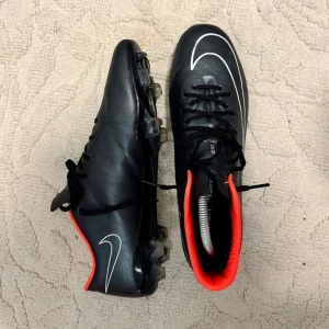 Nike Mercurial svarta fotbollsskor - Svarta Nike Mercurial fotbollsskor med vit swoosh och orange insida. Grässkor. Fråga om du undrar något!