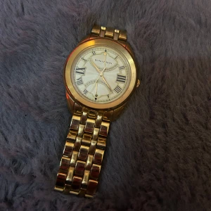 Guldfärgad klocka från Romanson - Stilren guldfärgad klocka från Romanson med klassisk länkarmband och rund urtavla. Urtavlan är ljus med romerska siffror och eleganta visare. Perfekt accessoar för dig som gillar en tidlös och lyxig look.