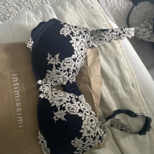 Svart spetsblus från Intimissimi - Supersnygg svart bh från Intimissimi med lyxiga spetsdetaljer i beige. Bh-n har blommigt broderi över hela framsidan och axelbanden, vilket ger en romantisk och trendig look. Använd men fortfarande i ett fint skick, storlek 75b. skicket är mellan bra och lagom mycket bra. Säljer för den är förstår och köpte en ny i min storlek, vid fler bilder skriv privat 🩷🩷