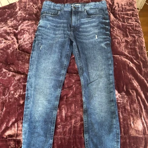 Blå skinny jeans från Calvin Klein - Snygga blå skinny jeans från Calvin Klein med klassisk femficksdesign och diskret CK-logo på myntfickan. Jeansen har slitningar och ljusare partier för en cool, använd look. Perfekta till sneakers. 98cm och 72cm i längd 