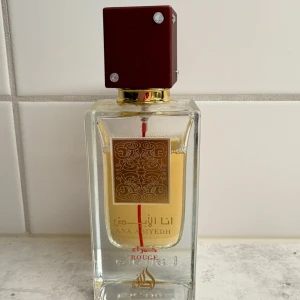 Ana Abiyedh Rouge parfym från Lattafa - Ana Abiyedh Rouge från Lattafa är en Eau de Parfum i en stilren, fyrkantig glasflaska med gulddetaljer och en mörkröd, kubformad kork med små stenar. Parfymen har en gyllene vätska och flaskan pryds av arabiska och engelska texter i guld. Väldigt lik baccarat rouge doften.