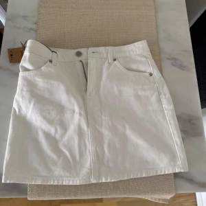 Vit jeanskjol från Forever 21 - Säljer en vit jeanskjol från Forever 21 med klassisk femficksdesign och bälteshällor. Den var tyvärr för liten för mig när jag beställde den. Kjolen har dragkedja och knapp framtill och är i en kort modell. Perfekt att matcha med en enkel topp eller hoodie.