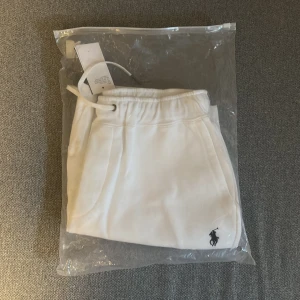 Vita shorts från Polo Ralph Lauren - Fräscha vita shorts från Polo Ralph Lauren med klassisk broderad logga i svart. Modellen har elastisk midja med snörning, sidofickor och en bakficka. Perfekta för sommaren och riktigt clean look. Materialet är mjuk bomull som känns skönt mot huden.