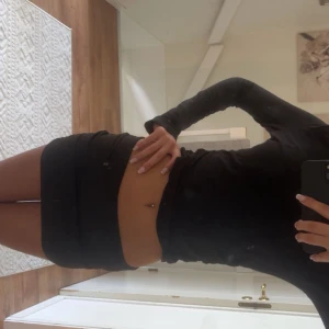 Svart tight kortkjol i stretch - Svart tight kortkjol med stretchigt material och enkel design. Kjolen sitter lågt i midjan och har shorts insytt under. Perfekt för dig som gillar en clean och stilren look. Den är väldigt stretchig så skulle säga att den hade passat S kanske M