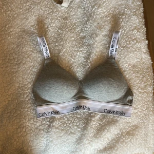 Grå bh från Calvin Klein - Fint skick, säljer pga fel storlek. Mjuk bomullskänsla och bekväm passform. Justerbara axelband och hakknäppning bak. Enkel och stilren design.