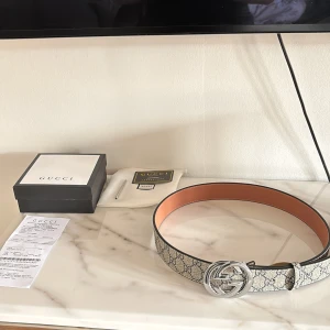 Beige Gucci bälte - Säljer ett GG bälte med klassiskt monogrammönster i beige och grått. Bältet har en stor rund silverspänne med GG-logga och insida i ljust skinn. Allt i bilderna medföljer. Perfekt accessoar för att lyfta din outfit med en lyxig touch!!! Hör gärna av dig vid funderingar och frågor🙌🏼. Pris är ej hugget i sten och kan sträcka mig väldigt långt till ett bra pris✅👍🏼. Skicket är som nytt