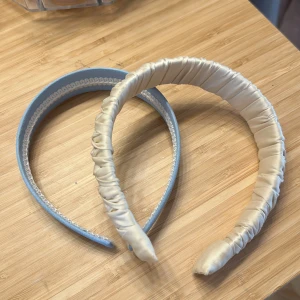 2-pack diadem i satin och blått tyg - Säljer två snygga diadem – ett i ljusblått tyg med vit kant och ett i glansig, champagnefärgad satin med coolt rynkat tyg. Perfekta accessoarer för att lyfta din look och hålla håret på plats.                      Kontakta mig om du har någon fråga ❤️
