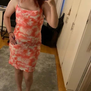 Rosa och vit långklänning med mönster - Säljer en långklänning i rosa och vitt med ett unikt mönster som påminner om moln eller batik. Klänningen är ärmlös och har en lös passform med rundad halsringning. Perfekt för sommarens varma dagar. Bilden är ungefär ett år gammalt har itne haft på den sedan dess