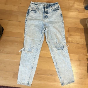 Acid wash ljusa ripped jeans - Säljer ett par ljusa acid wash jeans med hög midja och raka ben. Byxorna har slitna detaljer och hål på båda benen för en cool, avslappnad vibe. Klassisk femficksmodell och knappgylf. Perfekta för dig som gillar streetstyle.