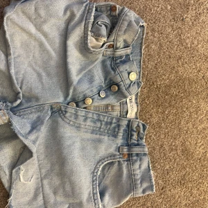 Ljusblå jeansshorts från Zara - Säljer ett par ljusblå jeansshorts från Zara med råa kanter och klassisk femficksdesign. Shortsen är midwaist! Skriv för bild på osv!