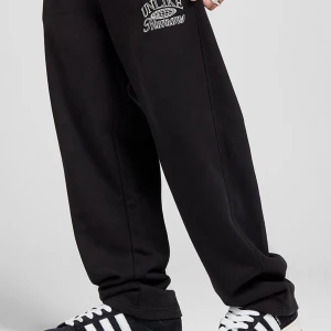 Svarta mjukisbyxor Unlike Humans - Svarta mjukisbyxor från Unlike Humans med broderad vit logga på ena benet. Byxorna har elastisk midja och en loose passform, perfekta för en chill och avslappnad stil. Tillverkade i mjuk bomull för maximal komfort.
