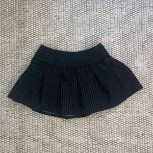 Kritstrecksrandig minikjol - Minikjol i svart med tunna vita ränder från pull&bear. Stretchig, så du kan välja om du vill ha högmidjad eller lowwaist 🫶🏻 storlek XS-S. Material 79% polyester, 15% viskos, 6% elastan ⭐️