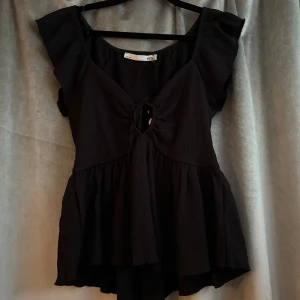 Svart blus med volangärm och knyt - Supersöt svart blus från 157 med volangärmar och v-ringning. Den är aldrig använd och prislappen sitter kvar.