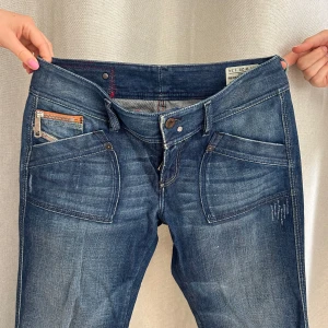 Blå diesel jeans  - Så snygga diesel jeans med coola detaljer och slitningar. Midjemåttet rakt över: 40cm och står W29 på lappen. Innerbenslängd: 90cm och modellen på bilden är 1,68cm lång.