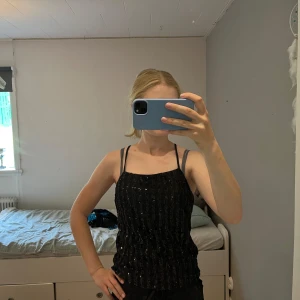 Svart paljettlinne från Bik Bok - Säljer ett svart linne från Bik Bok med smala axelband och glittriga paljetter över hela toppen. Sitter tight och har en snygg, rak halsringning. Perfekt för att sticka ut och ge outfiten extra bling.