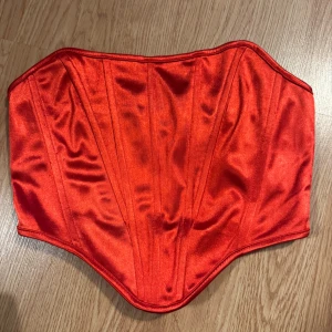 Röd satin korsett topp - Snygg röd korsett topp i glansigt satinmaterial med markerade sömmar för en siluett. 