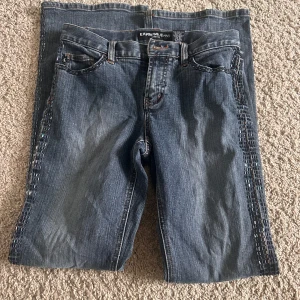 Blå Express Jeans med paljettdetaljer - Snygga blå jeans från Express Jeans med stretch och coola paljettdetaljer längs sidorna. Modellen är croppad och har klassisk femficksdesign. Materialet är 98% bomull och 2% spandex för skön passform. Perfekt för dig som vill sticka ut lite extra.