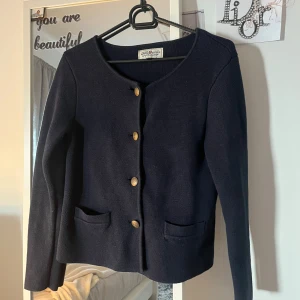 Mörkblå stickad cardigan jacka - Snygg mörkblå stickad cardigan jacka från hampton republic. Koftan har guldiga knappar framtill, två små fickor och en klassisk rund halsringning. Kommer längre inte till användning 