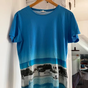  Orlebar Brown tshirt med strandmotiv - Snygg blå t-shirt från Orlebar Brown med strand- och poolmotiv tryckt över hela nederdelen. T-shirten har rund hals, korta ärmar och är gjord i mjuk bomull. Perfekt för dig som gillar unika prints och sommarvibes.