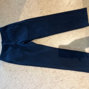 Mörkblå fleecebyxor från H&M - Mysiga mörkblå fleecebyxor från H&M med regular fit. Byxorna har resår i midjan och dragsko för skön passform. Perfekta för chill eller när du vill vara extra bekväm. Klassisk rak modell utan synliga detaljer.