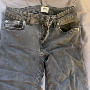 Svarta bootcut jeans från 157 - Säljer ett par svarta jeans från 157 med klassisk femficksdesign och bootcut-ben. Jeansen har knapp och dragkedja framtill samt bälteshällor. Materialet är jeans med en något tvättad look och raka sömmar. Perfekt för dig som gillar en avslappnad stil.