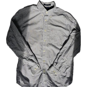 Randig skjorta från Tommy Hilfiger - Snygg skjorta från Tommy Hilfiger i vitt och blått med klassiskt randigt mönster. Skjortan har lång ärm, knappar framtill och en bröstficka med liten logga. Tillverkad i bomull för en skön känsla och stilren look.