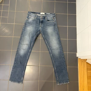 Replay Grover straight fit jeans blå - Säljer ett par Replay Grover straight fit jeans i klassisk blå tvätt med snygga slitningar. Jeansen har raka ben, normal passform och gul kontrastsöm på bakfickorna. Perfekt för dig som gillar tidlös stil och vill ha ett par jeans som funkar till allt.