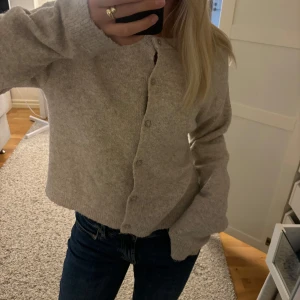 Beige stickad kofta med knappar - Mysig beige stickad kofta med rund hals och knäppning framtill. 