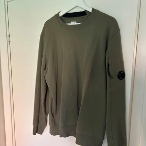 Olivgrön sweatshirt från C.P. Company - Säljer en olivgrön sweatshirt från C.P. Company. Tröjan har rund hals, ribbade muddar och är tillverkad i mjuk bomull. 